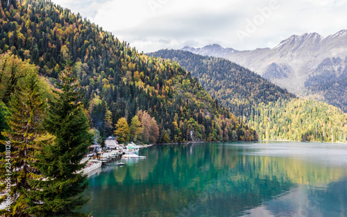 Caucasus. Abkhazia. Riza lake, autumn forest and white snow peaks, reflecting in the calm water of the lake.