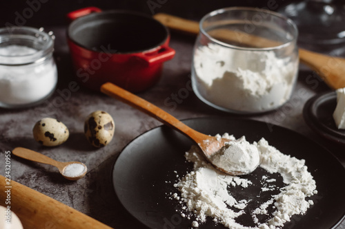 Ingredients and utensils for baking. Spoon with flour, dishes, eggs, butter salt and rolling pin on a grey background. Flat lay. 