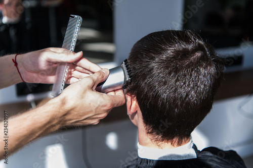 Perfect trim. Rear view close-up of young man getting haircut by hairdresser with electric razor.