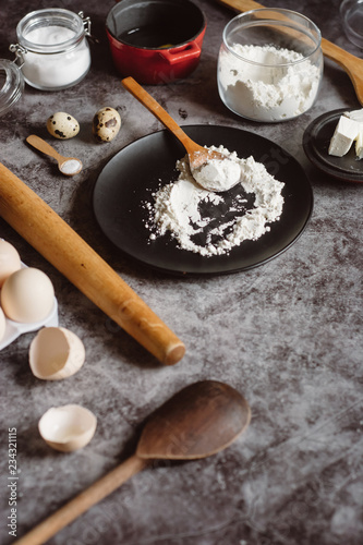 Ingredients and utensils for baking. Spoon with flour, dishes, eggs, butter salt and rolling pin on a grey background. Flat lay. Text space
