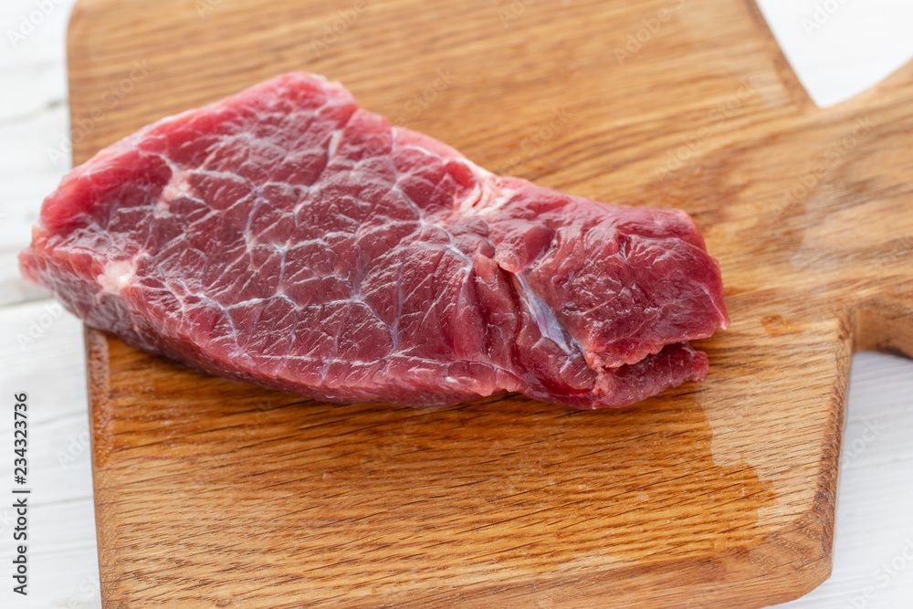 Morning in the kitchen. Raw meat. Raw fresh beef steak on a wood cutting board. White wooden background, top view, copy space, Daylight Morning in the kitchen. Raw meat. Raw fresh beef steak on a wood cutting board. White wooden background, top view, copy space, Daylight