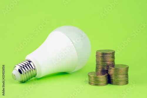 energy saving lamp and coins on green background. Efficient energy use, using less energy reduces energy costs concept