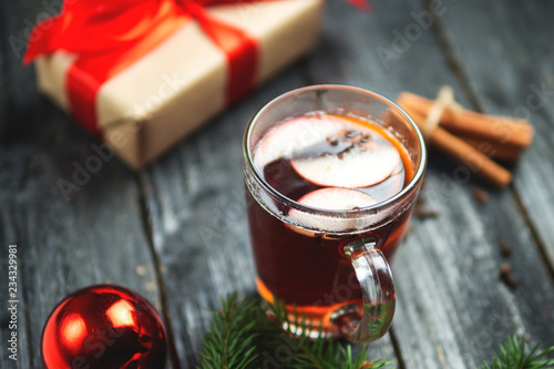 Hot wine with a gift box on a dark wooden table. Traditional drink for the holiday