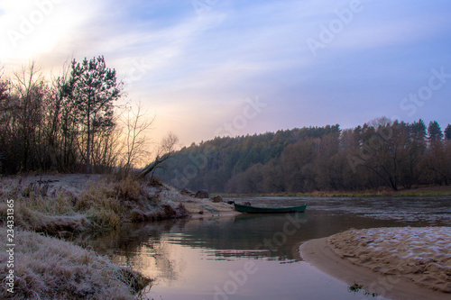 landscape by the river: a wooden boat at the shore and the first frost