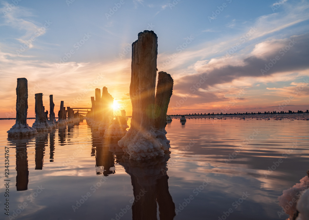 sunset on a pink salt lake, a former mine for the extraction of pink salt. row of wooden pegs overgrown with salt.