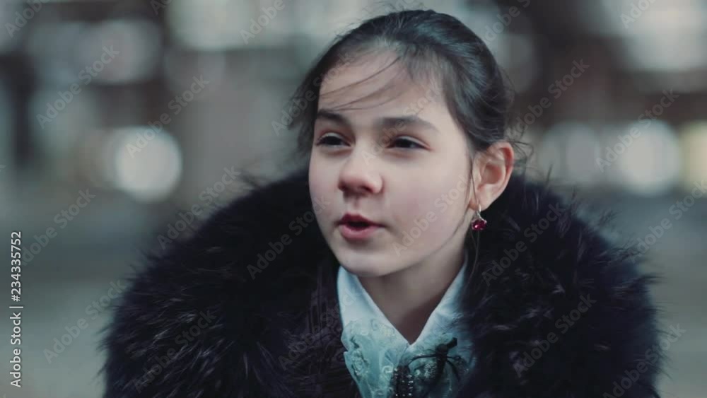 Pretty little Caucasian girl with dark hair looking away. Portrait of cute speaking schoolgirl in elegant clothes. Outdoors. Close-up. Pretty little Caucasian girl with dark hair looking away. Portrait of cute speaking schoolgirl in elegant clothes. Outdoors. Close-up.