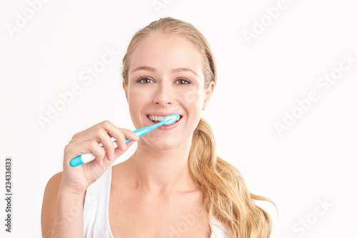 Beautiful young woman brushing her teeth against white background