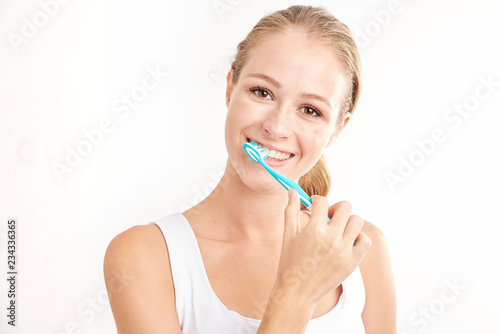 Beautiful young woman brushing her teeth against white background