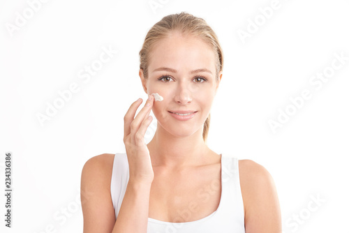 Foto Young woman applying face cream against white isolated background