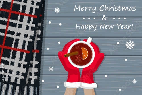 Hands in Christmas mittens hold mulled wine and plaid lying on table