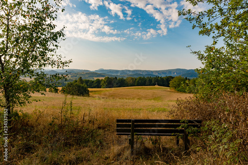 A cosy bench, waiting for a hiker, with a beautiful view over meadows and fields.