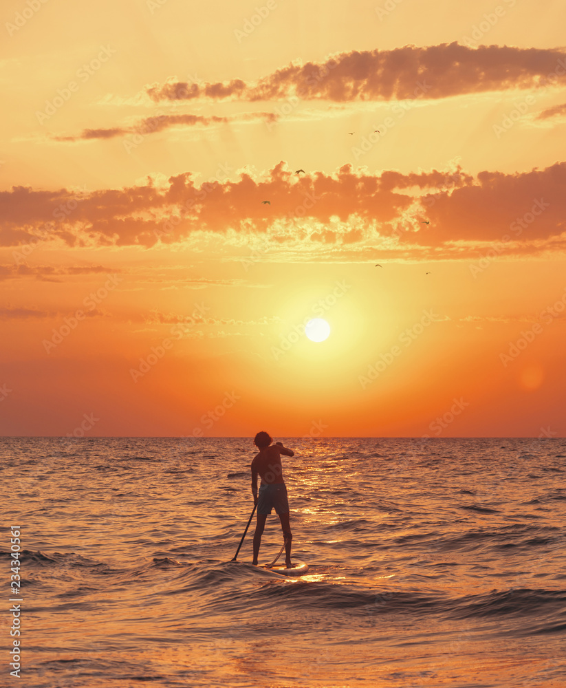 Man paddling on a SUP board in the sea at sunset.