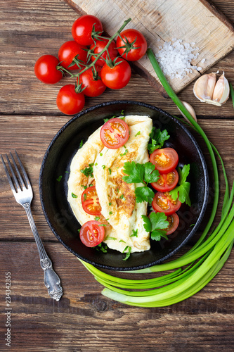 Omelet with cherry tomatoes and fresh green parsley in a black iron pan on a wooden background.