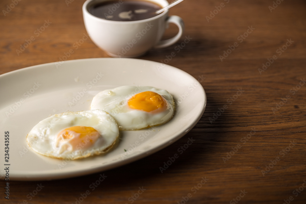Fried Eggs on white plate and cup of black Coffee for Breakfast on wooden background Fried Eggs on white plate and cup of black Coffee for Breakfast on wooden background
