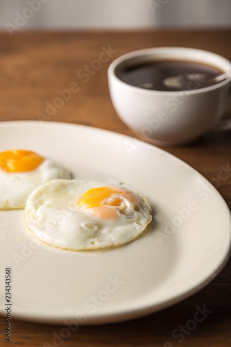 Fried Eggs on white plate and cup of black Coffee for Breakfast on wooden background