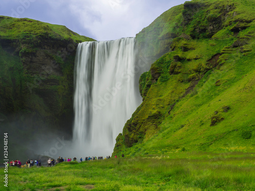 Beautiful Skogafoss waterfall in South Iceland Skogar with group of colorful dressed tourist people, long exposure motion blur