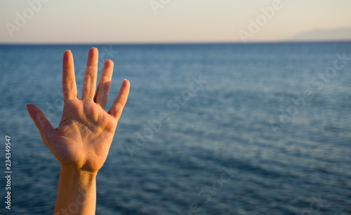 Woman's hand isolated on blue background in summer sea nature. Stop, help, fifth concept with hand up. Gesture symbol number five in sign language. Say hello / hi or goodbye concept with copy space.