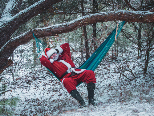 Santa Claus lies in the hammock in the snow-covered winter forest. Christmas vacation in nature.