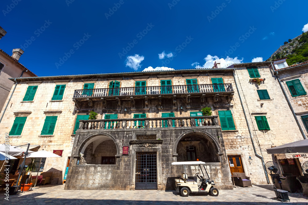 Old stone house with beautiful relief balconies and green shutters for windows, a small servicing golf car next to the house. Pima Palace, Kotor Old Town, Montenegro - August 2014.