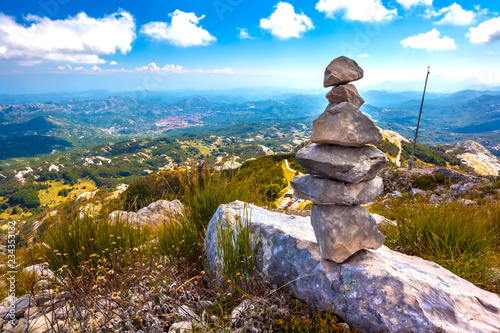 Stone cairns pyramid built on top of a mountain with a panoramic view of the Montenegrin valley of hills and forests under a blue sky with white clouds. Vidikovac, Lovcen National Park, Montenegro. photo