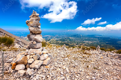Stone cairns pyramid built on top of a mountain with a panoramic view of the Montenegrin valley of hills and forests under a blue sky with white clouds. Vidikovac, Lovcen National Park, Montenegro. © Valery Bocman