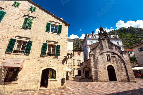 The ancient church on the square in the beautiful stone city between the amazing buildings among the mountains in the summer cloudless weather. Saint Lukas Church, Kotor Old Town, Montenegro. © Valery Bocman