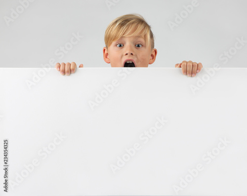 little blond boy holds a placard in his hand, with mouth open