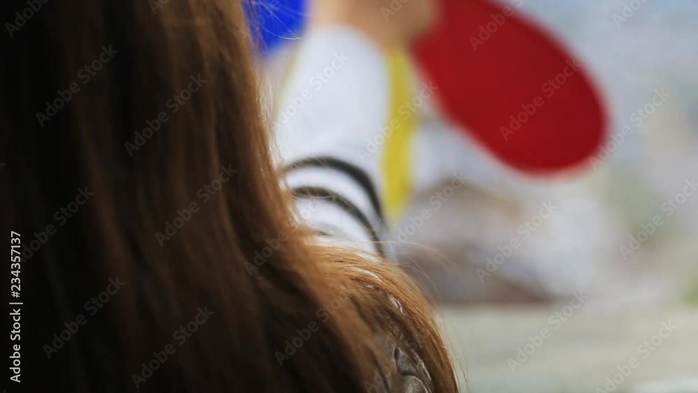 Back shot of schoolgirl with straight brown hair. Girl holding colored vane in hand in background of town. Outdoors, close-up. Back shot of schoolgirl with straight brown hair. Girl holding colored vane in hand in background of town. Outdoors, close-up.