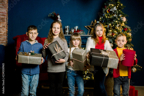 Happy group of Kids holding Christmas gifts  on the background of Christmas decorations in cozy nice room.