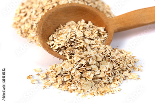 Heap of rolled oats with wooden spoon on white