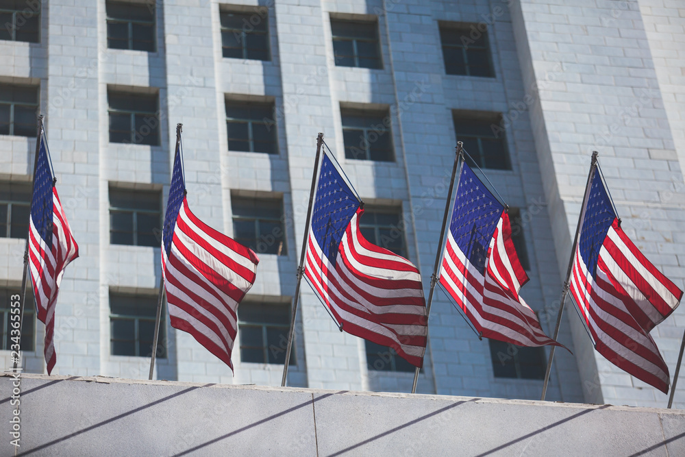 View of waving American flag in the wind with beautiful blue sky in background, line of United States of America Flags