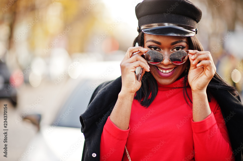 African american fashion girl in coat, newsboy cap and sunglasses posed at street against white business car.