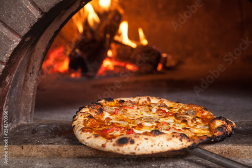 Pizza pie being taken out of a wood burning oven