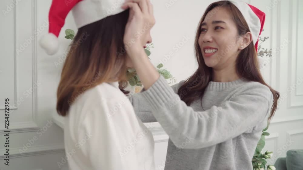 Lesbian Asian couple giving and wear christmas hat to each other in her living room at home in Christmas Festival. Lifestyle lgbt women happy celebrate Christmas and New year concept. Lesbian Asian couple giving and wear christmas hat to each other in her living room at home in Christmas Festival. Lifestyle lgbt women happy celebrate Christmas and New year concept.