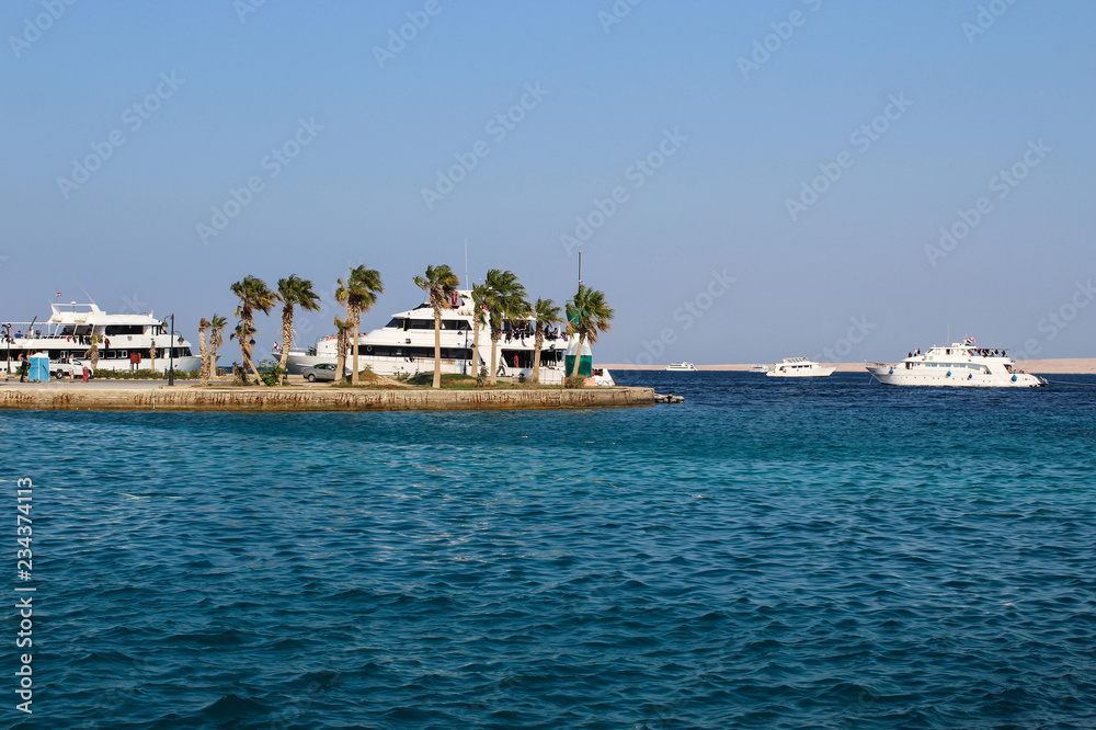 Passenger ships in the sea harbor of Hurghada, Egypt. Tourist boats and yachts on the background of palm trees and Red Sea.