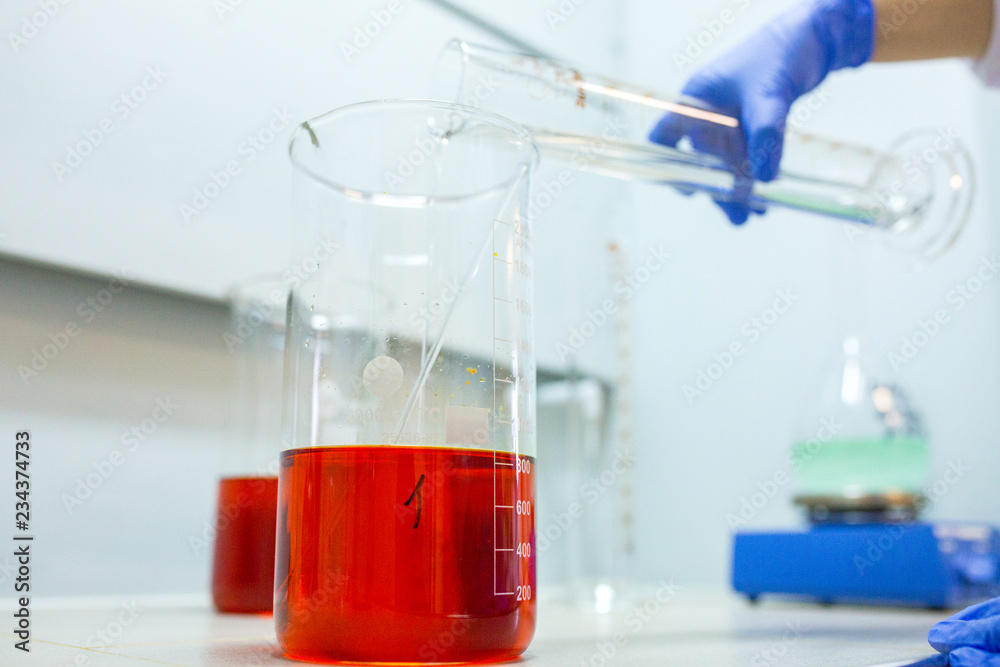 Hands of the scientist in the laboratory mixes with transfusion a chemical materials from graduated cylinder to beaker. Concept theme of applied chemistry - reaction, compound, solutions, dilution. Hands of the scientist in the laboratory mixes with transfusion a chemical materials from graduated cylinder to beaker. Concept theme of applied chemistry - reaction, compound, solutions, dilution.