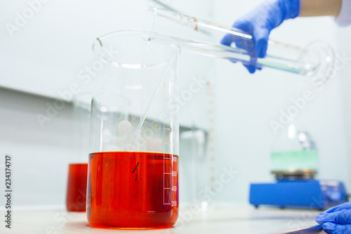 Foto Hands of the scientist in the laboratory mixes with transfusion a chemical materials from graduated cylinder to beaker