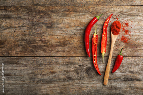 Flat lay composition with fresh chili peppers, powder and space for text on wooden background