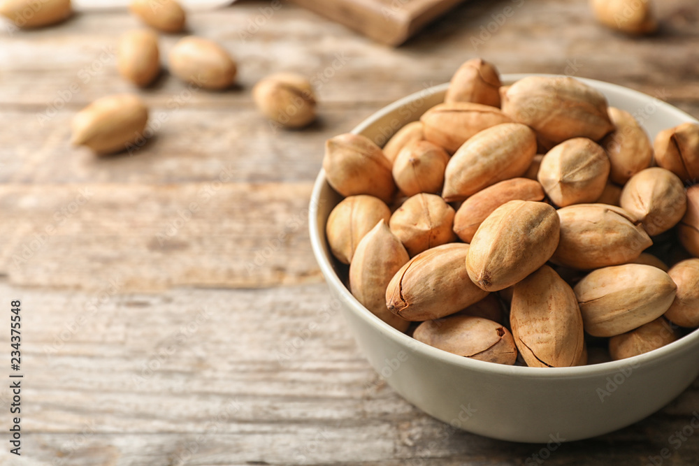 Pecan nuts in bowl on wooden table, space for text