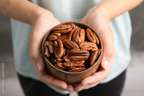 Woman holding bowl with shelled pecan nuts in hands, closeup