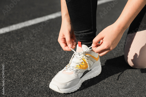 Young woman tying shoelaces at stadium on sunny day