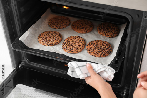 Young woman taking baking sheet with cookies from oven, closeup