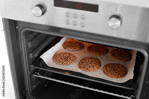 Open modern oven with freshly baked cookies on sheet in kitchen