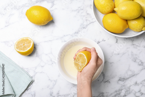 Woman squeezing lemon juice into bowl on table, top view