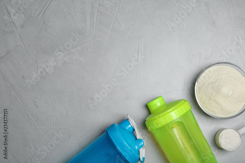 Bottles, protein powder and space for text on grey background, top view. Preparing shake