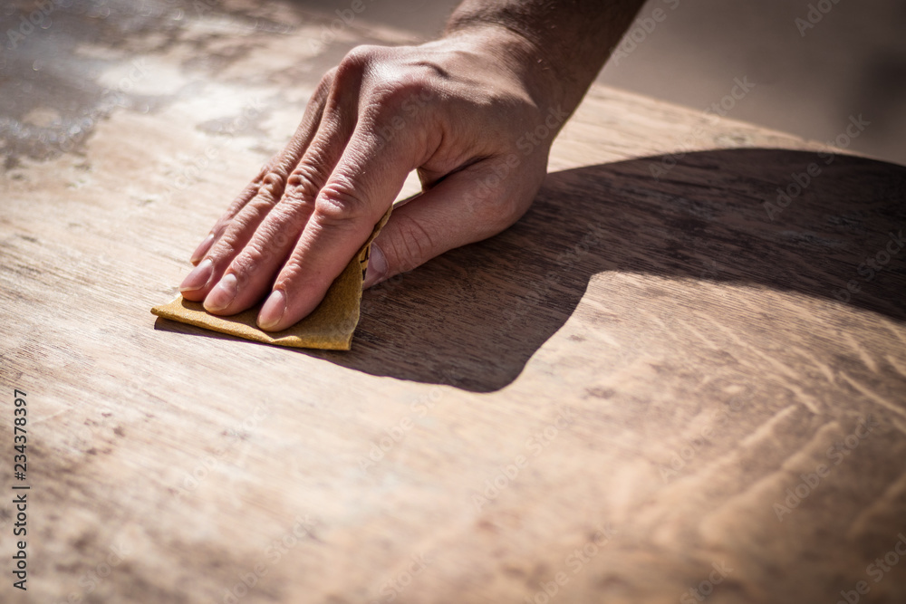 Gritty weathered man's hand and sandpaper; hand sanding a table top to refinish with paint or stain