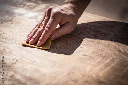 Gritty weathered man's hand and sandpaper; hand sanding a table top to refinish with paint or stain