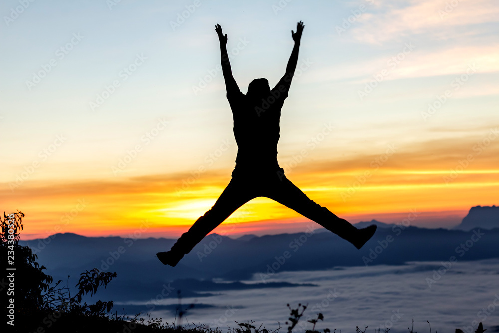 Silhouette of happy man jumping with raised hands at sunset or sunrise time