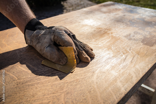 Hand in glove with sandpaper; sanding a table top to refinish with paint or stain