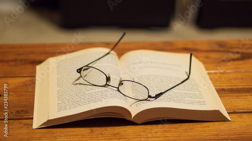 Eye glasses resting on top of a book, sitting on a wooden coffee table